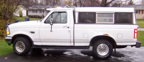 1978 Ford Bronco - Side view of a white Ford F-150 pickup truck equipped with a camper shell. The vehicle shows some signs of rust.