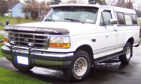 1978 Ford Bronco - A white Ford pickup truck with a camper shell is parked on a wet driveway.