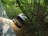1989 GMC Jimmy - A white SUV navigates a challenging off-road trail through a dense forest.