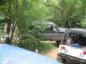 1989 GMC Jimmy - A weathered pickup truck sits beside a trailer, partially obscured by trees and foliage.