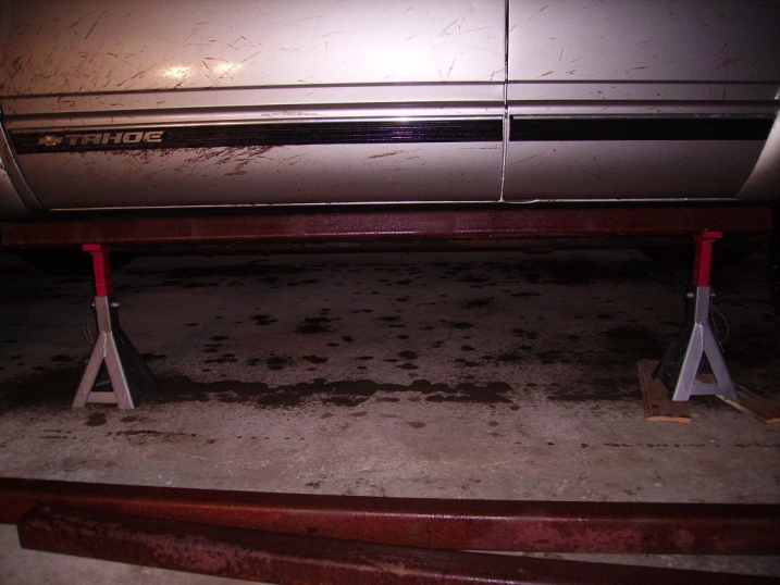Side of a Tahoe on jack stands. The vehicle is silver with a black stripe and the word TAHOE is visible