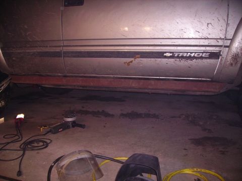 2000 Chevrolet Tahoe - The side of a silver 2000 Chevrolet Tahoe is visible, with a 'TAHOE' badge and some rust on the lower body panel.
