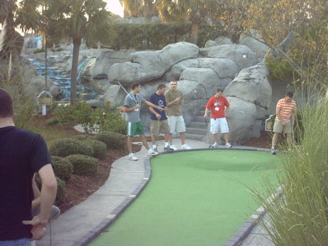 1997 Ford Probe - A group of friends enjoys a game of mini golf on a sunny day, with a decorative waterfall and rocky landscape.