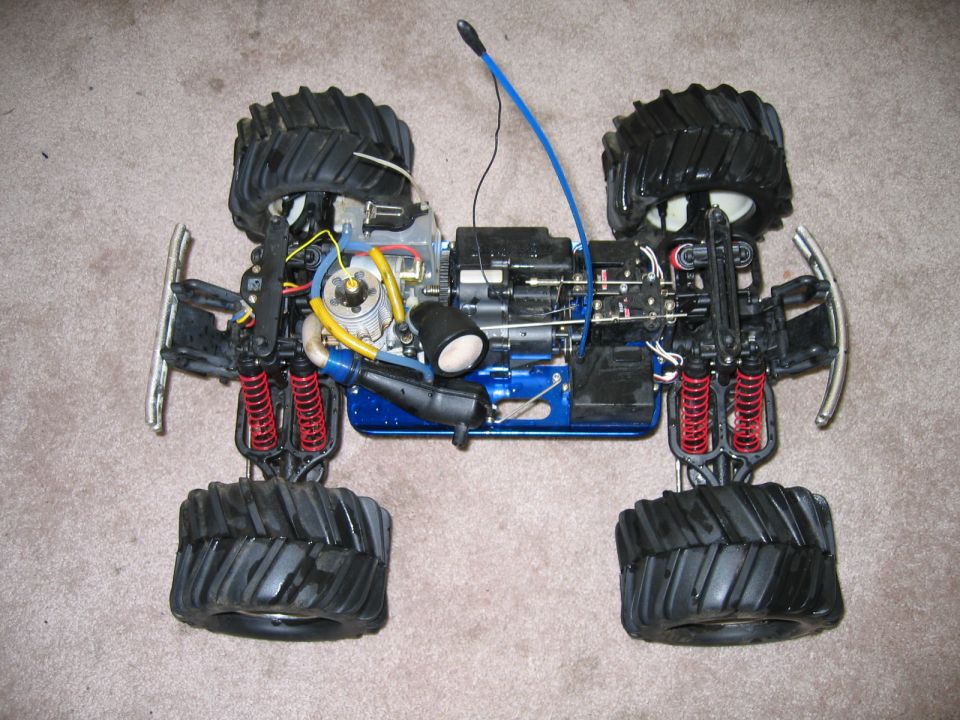 RC monster truck chassis with engine, shocks, and large tires. Blue frame