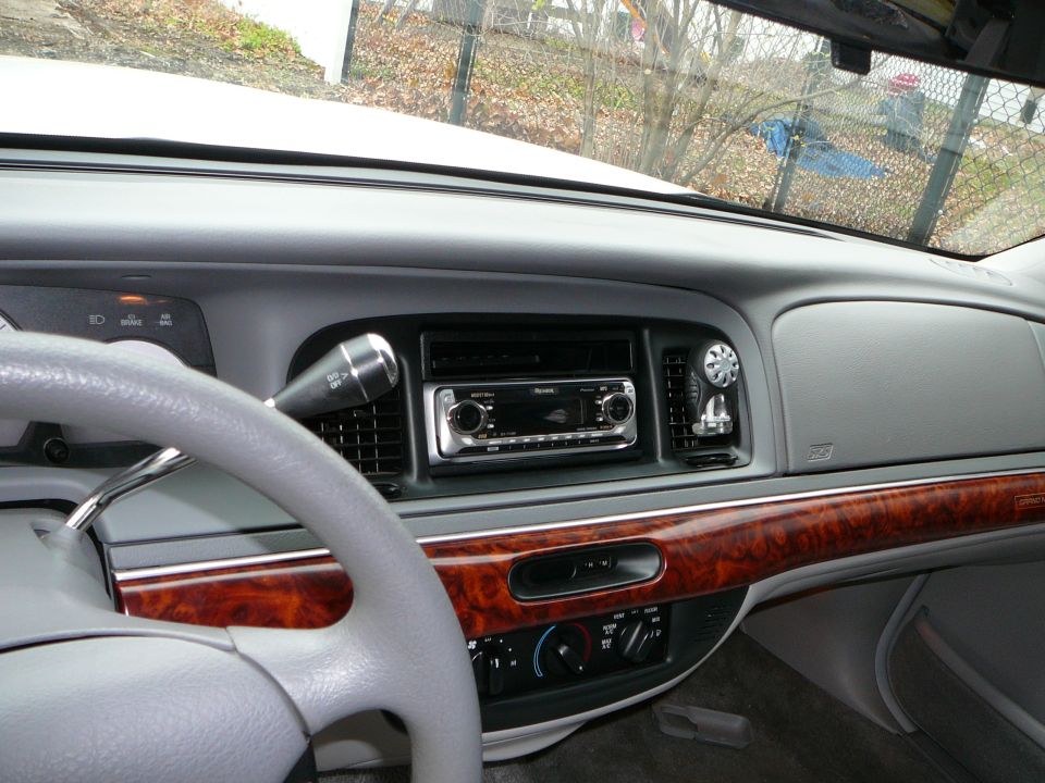 Car interior showing dashboard, steering wheel, and aftermarket stereo. Wood trim accents the center console