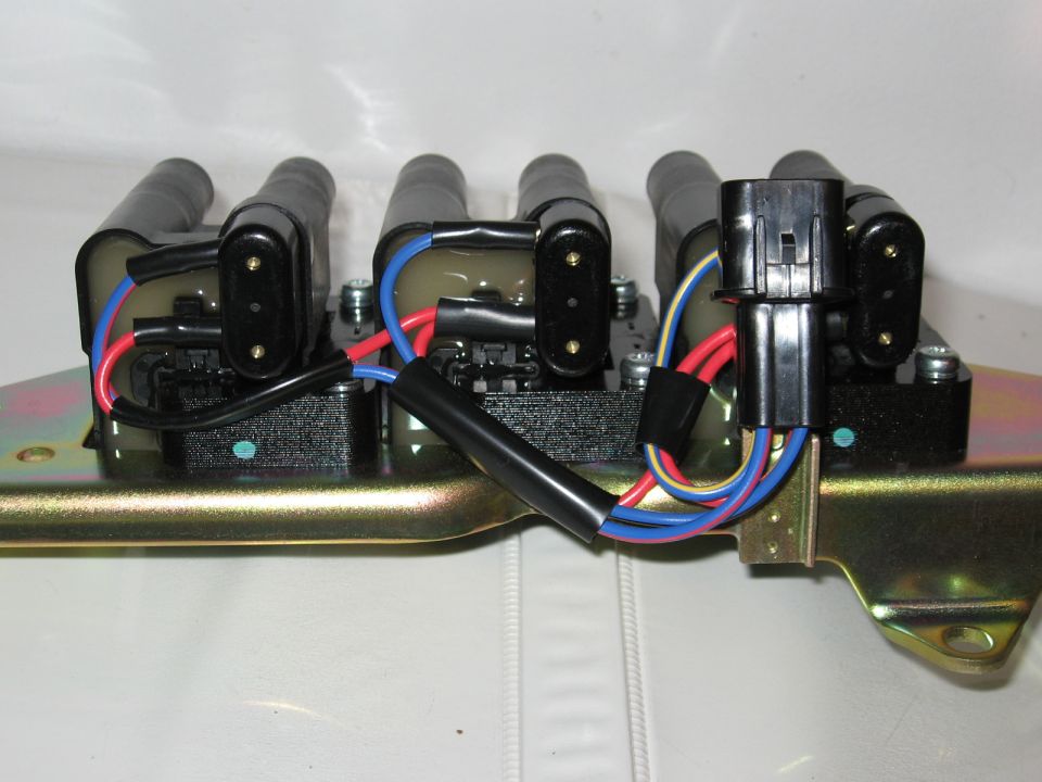 Ignition coil pack with three coils and colored wiring on gold zinc-plated bracket, off the car