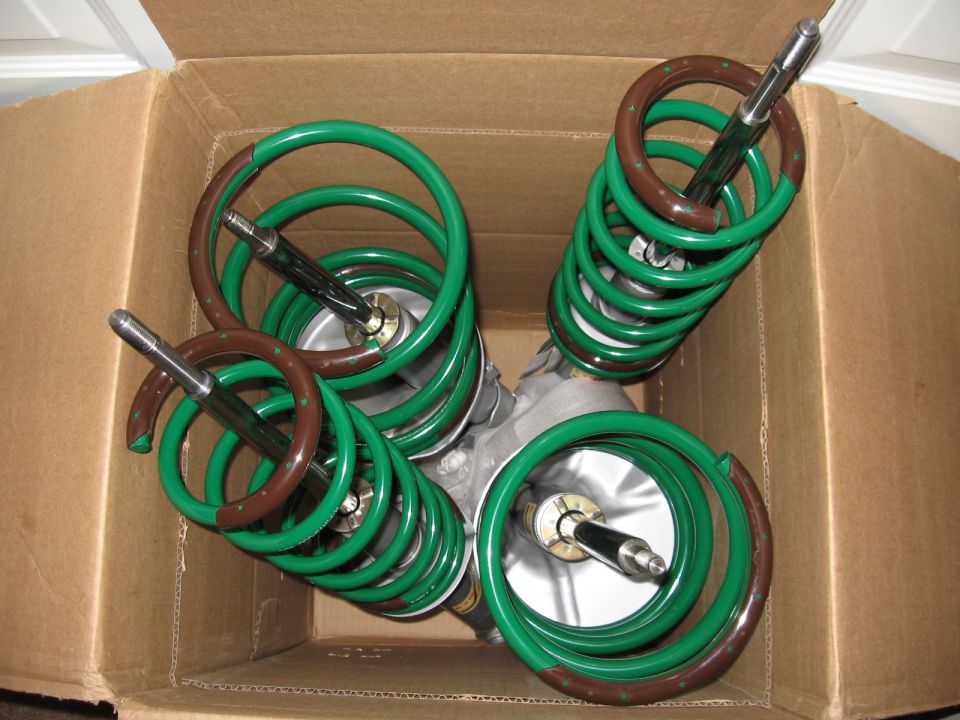 Four coilover struts with green springs packed in a cardboard box