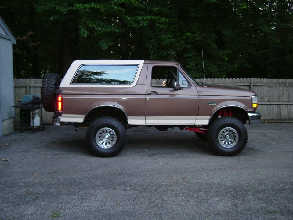 Brown and tan lifted Ford Bronco SUV parked in profile on gravel driveway