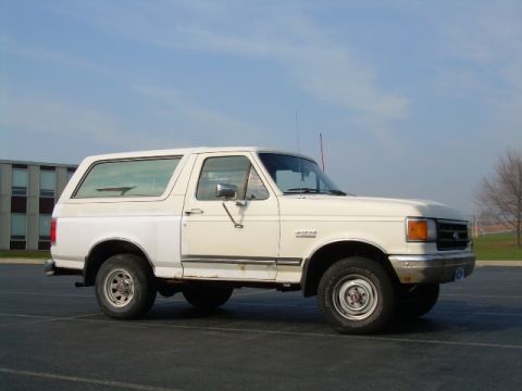 1988 Ford Bronco - This two-tone Ford Bronco is parked in an empty lot with a building in the background.