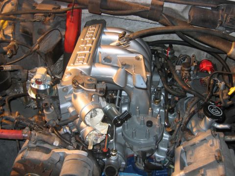 1992 Ford Bronco - Top-down view of a freshly repainted silver V8 engine bay, showing a Ford intake manifold, distributor cap with plug wires, a black oil-fil…