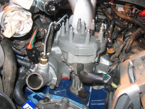 1992 Ford Bronco - Close-up engine bay view of a gray plastic distributor cap with spark plug towers mounted centrally, surrounded by wiring harnesses, connec…