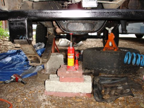 1989 Ford Bronco - The underside of a vehicle is shown with its rear end elevated for maintenance, a hydraulic jack and various tools.