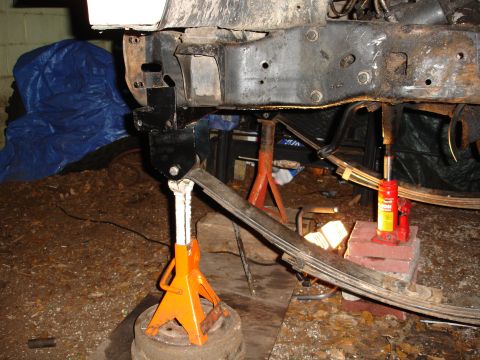 1989 Ford Bronco - Close-up view of vehicle frame and suspension components being supported by jack stands and a hydraulic jack during maintenance or modifica…