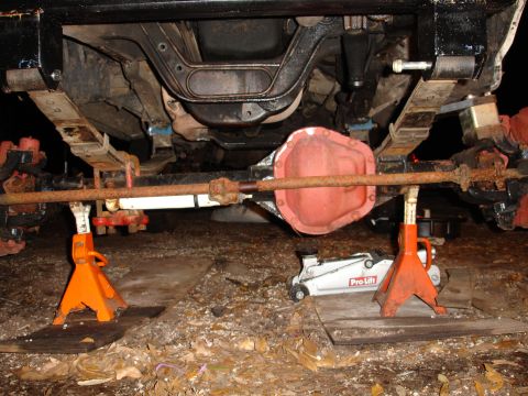 1989 Ford Bronco - The underside of a vehicle is supported by jack stands, revealing its suspension and drivetrain components.