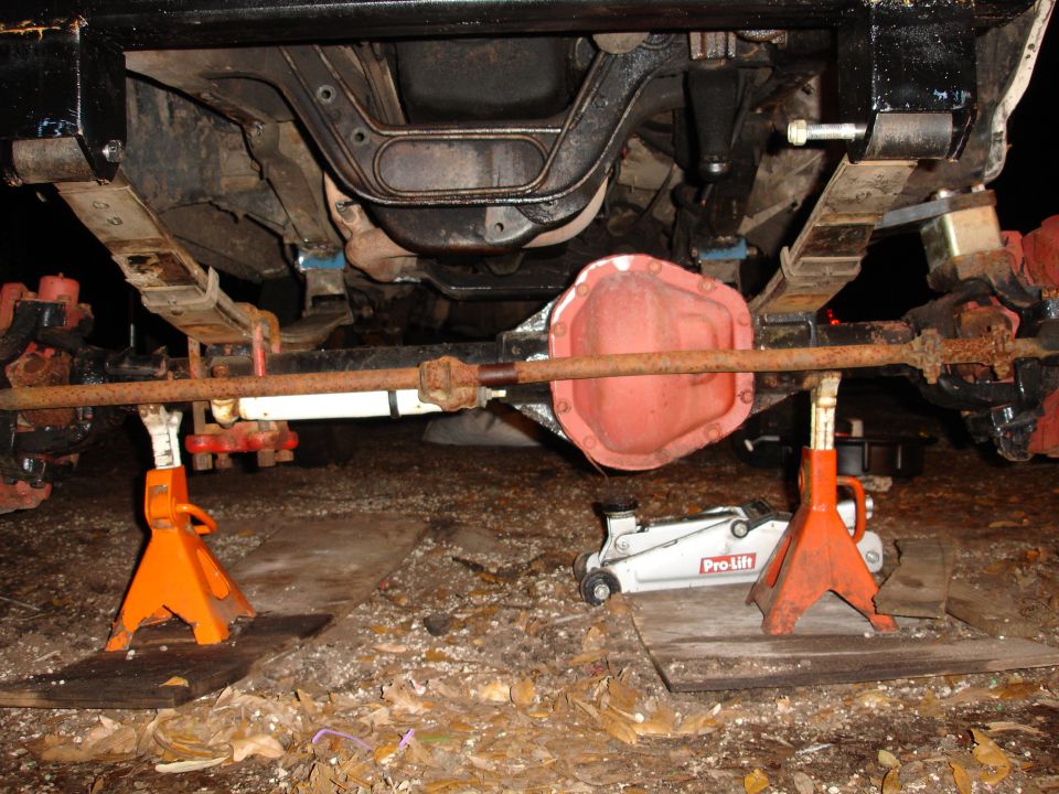Undercarriage of a vehicle on jack stands, showing leaf springs and differential