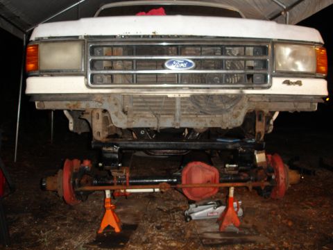 1989 Ford Bronco - Front view of a white Ford truck, likely from the late 1980s, with its front axle disassembled and supported by jack stands.