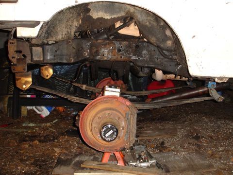1989 Ford Bronco - The rear suspension and brake assembly of a vehicle are visible, supported by jack stands.