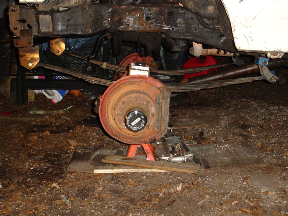 Rusty vehicle frame with leaf springs and brake rotor on jack stands