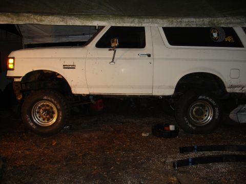 1989 Ford Bronco - A white Ford Bronco is shown from the side, parked under a tarp with its front wheel turned.