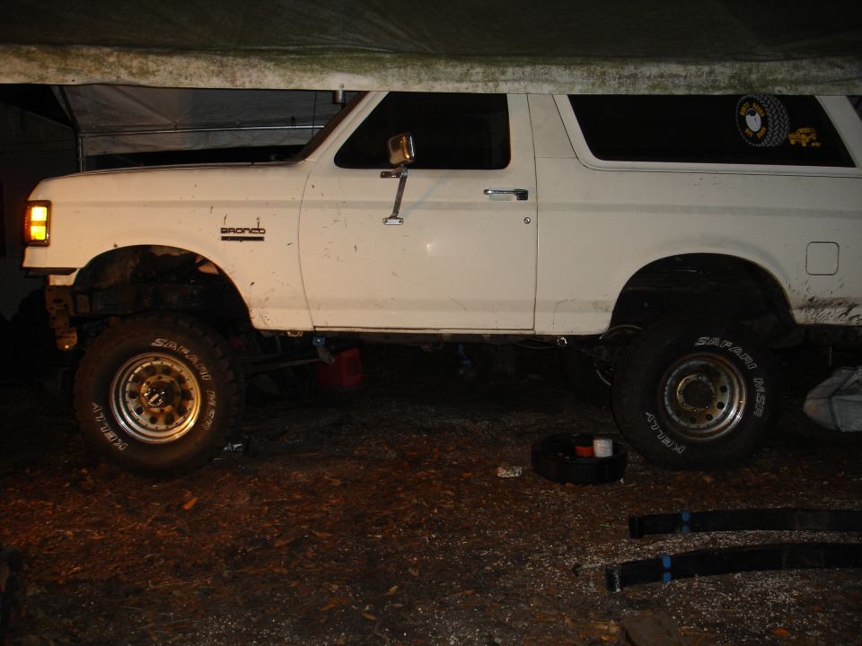 White Ford Bronco parked under a tarp, side view. Has 'Bronco' badge on fender