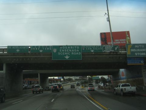 1990 Ford Bronco - Dashboard view of a highway passing beneath an overpass with green signs for Rosarito, Ensenada, and the Scenic Road.