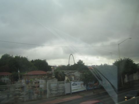 1990 Ford Bronco - view through a car window of a town with a tall white arch monument in the distance under a heavy overcast sky.