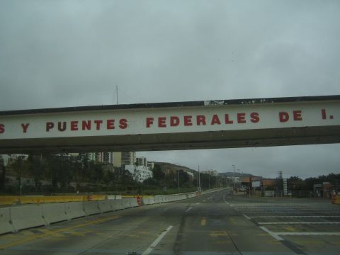 1990 Ford Bronco - large overhead gantry with red lettering reading '...y Puentes Federales de I...' spans an empty highway with hills in the background.