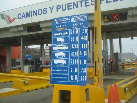 1990 Ford Bronco - toll plaza booth signed 'Caminos y Puentes' with a blue tariff board listing vehicle rates for Plaza de Cobro 35 Rosarito.