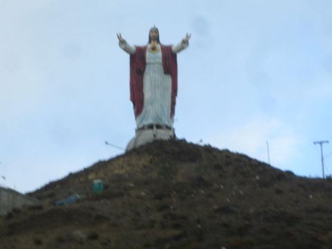 1990 Ford Bronco - large statue of a robed figure with arms outstretched, wearing white and red, stands atop a bare dirt hill under a pale sky.