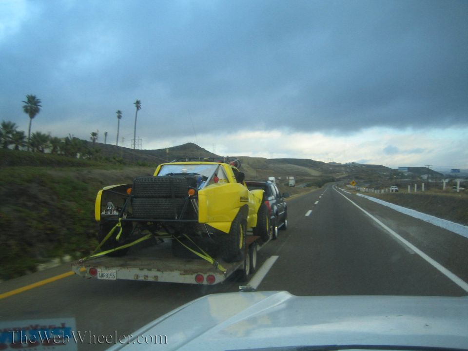Yellow off-road race buggy on a flatbed trailer towed down a coastal highway