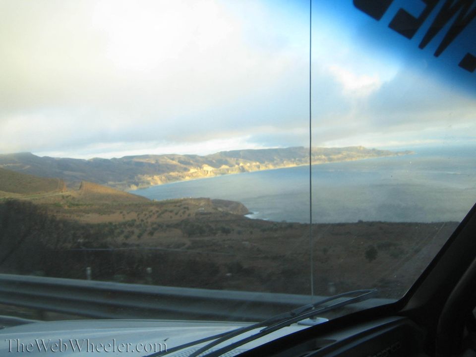 Coastal bay and hills viewed through a car windshield at low sun