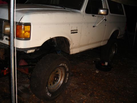 1989 Ford Bronco - A white 1989 Ford Bronco is shown with a lifted suspension and oversized tires, possibly undergoing modifications.