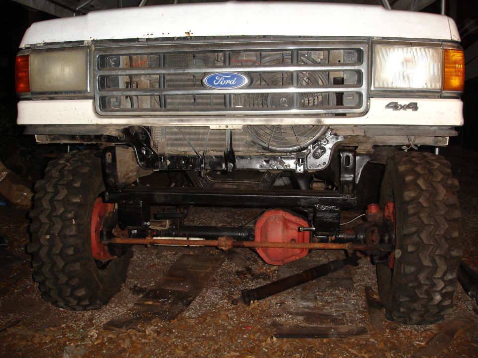 Front view of a white Ford truck with a custom grille and 4x4 badging. The chassis and suspension components are visible