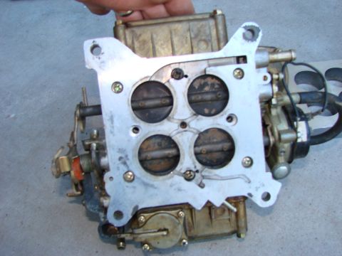 1979 Ford Bronco - A carburetor, likely for an I6 engine, is shown with its four throttle plates visible. The part is held by a hand against a concrete surfac…