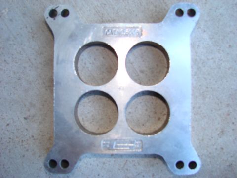 1979 Ford Bronco - This aluminum intake manifold spacer features four circular openings and a visible part number, likely for an engine modification.
