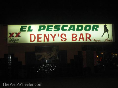 1990 Ford Bronco - lit nighttime storefront sign reads 'El Pescador Deny's Bar' with 'Floor Show' text, an XX Lager logo, and a dancer silhouette.