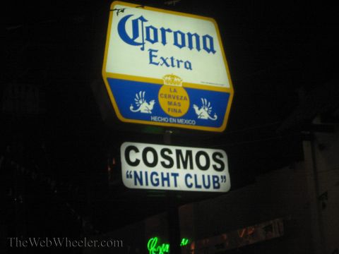 1990 Ford Bronco - lit Corona Extra beer sign hangs above a 'Cosmos Night Club' sign against a dark night sky.