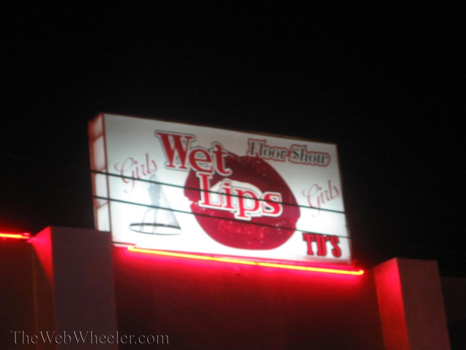 Illuminated red and white Wet Lips Floor Show sign glowing at night