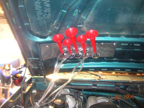 1996 Ford Bronco - Underhood view of a five-trumpet red musical air horn set bolted to a metal bracket mounted on the teal inner fender/cowl of a vehicle, wit…