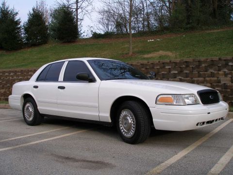 2001 Ford Crown Victoria - A white 2001 Ford Crown Victoria is parked in a lot, showing its front and side profile.