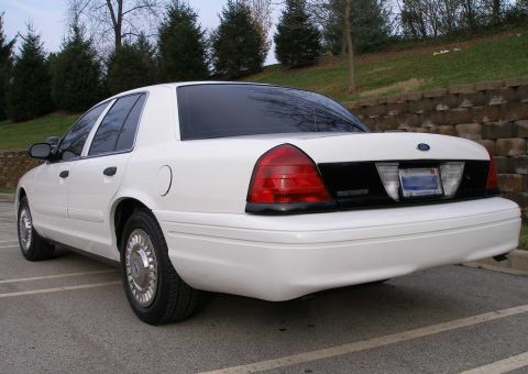 2001 Ford Crown Victoria - Rear view of a white sedan with tinted windows and chrome hubcaps parked in a lot.