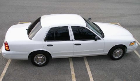 2001 Ford Crown Victoria - A white 2001 Ford Crown Victoria is shown from the side, parked in a lot with painted lines.