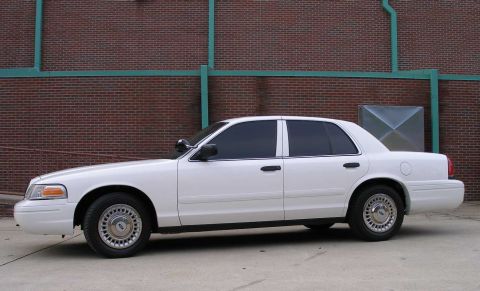 2001 Ford Crown Victoria - Side profile of a white 2001 Ford Crown Victoria sedan parked in front of a brick wall.