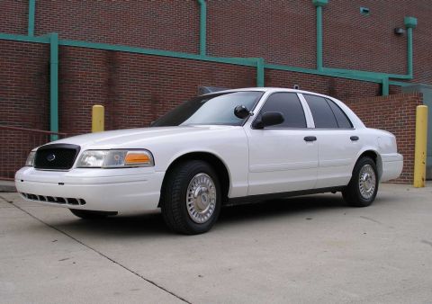 2001 Ford Crown Victoria - White 2001 Ford Crown Victoria sedan parked on concrete in front of a brick building.