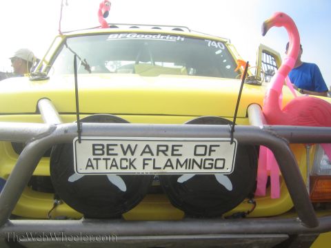1990 Ford Bronco - close-up of a yellow race truck's bull bar shows a 'Beware of Attack Flamingo' sign and pink flamingo decorations.