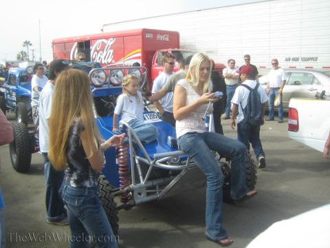 1990 Ford Bronco - People including a young woman gather around a blue open-frame off-road buggy in a paddock, with a Coca-Cola trailer behind.