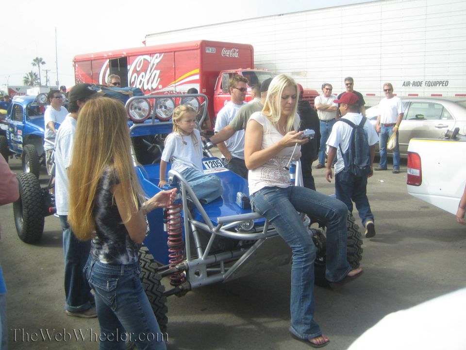 Blue off-road race buggy in a paddock with spectators and a Coca-Cola truck behind