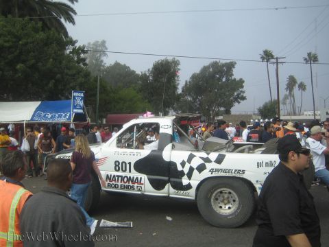 1990 Ford Bronco - white off-road race truck '801' with checkered-flag and 'got milk?' graphics sits in a street crowd at a racing event.