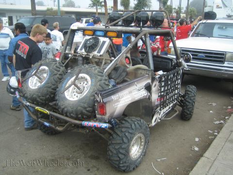 1990 Ford Bronco - Rear view of a tube-frame off-road race UTV carrying two spare tires, parked in a crowd at a contingency area.