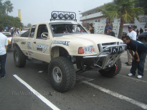 1990 Ford Bronco - tan single-cab Ford Ranger prerunner race truck with roof lights and Fiberwerx body panels staged on a street.